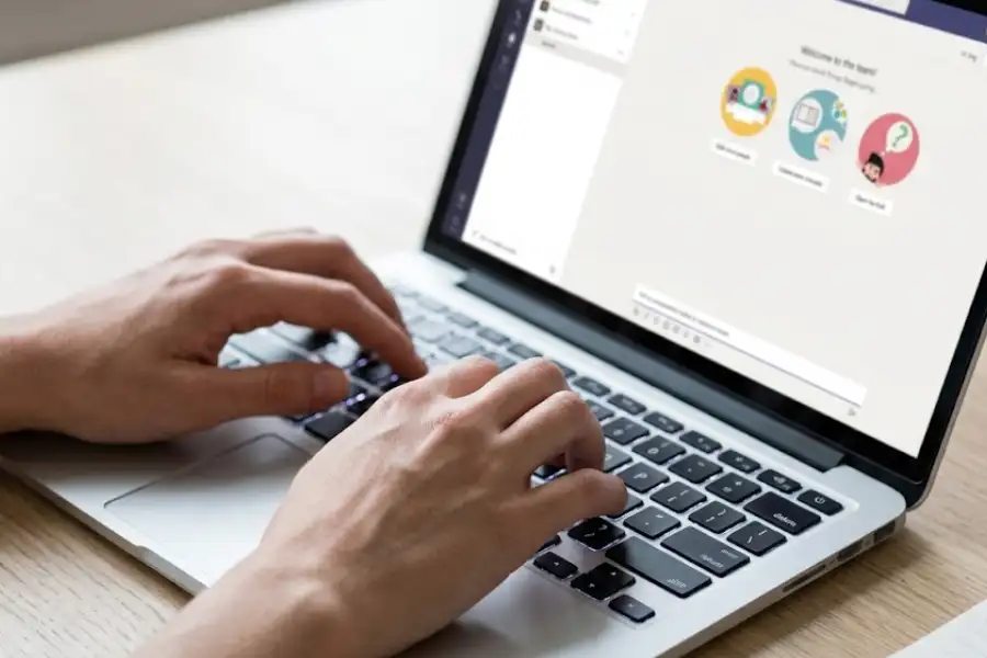 Close-up of hands typing on a laptop keyboard while using Microsoft Teams