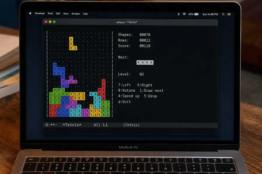 Close-up of a MacBook screen showing the Mac Terminal app with the Emacs Tetris game actively running, displaying falling text-based Tetromino blocks on the left and a score panel on the right