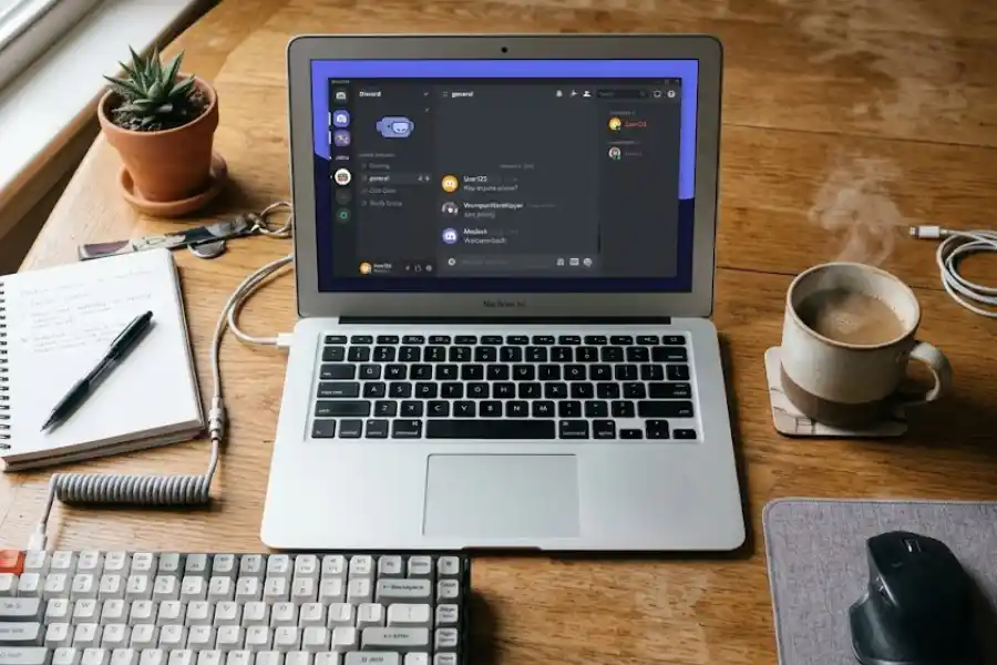 Close-up view of the Discord desktop app open on a laptop screen showing the Discord logo in the top left corner with a keyboard and coffee mug on the desk beside it