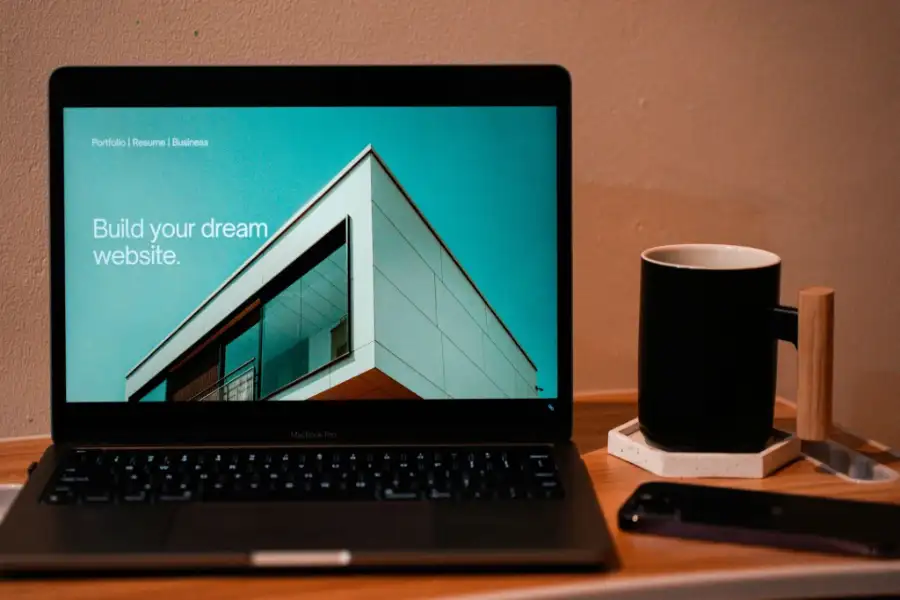 Laptop displaying a modern website design on a desk with a coffee mug and smartphone.
