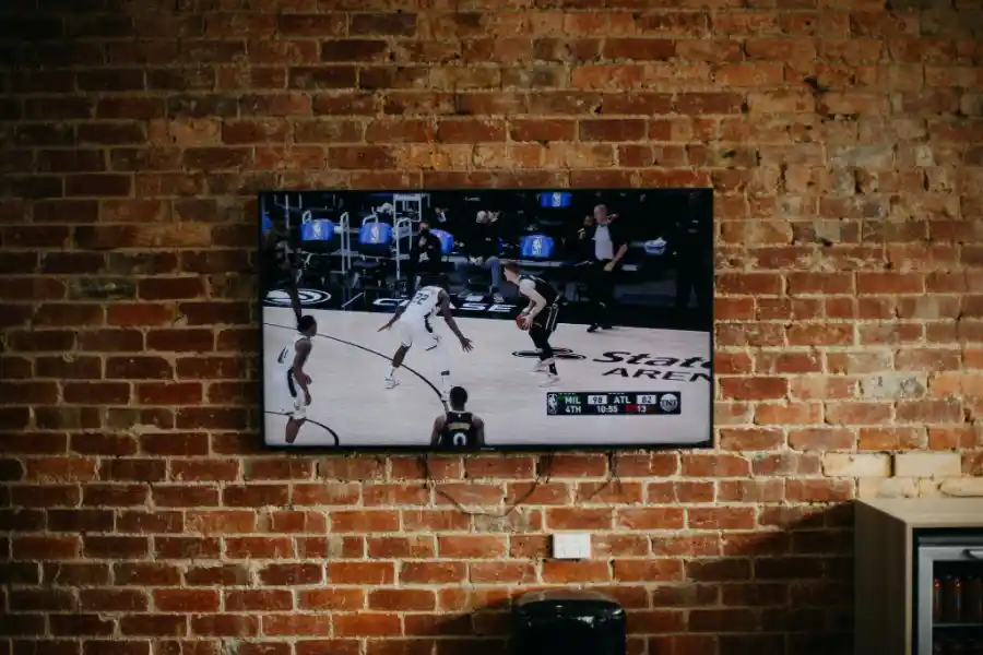 Wall-mounted TV displaying a live basketball game against a brick wall.