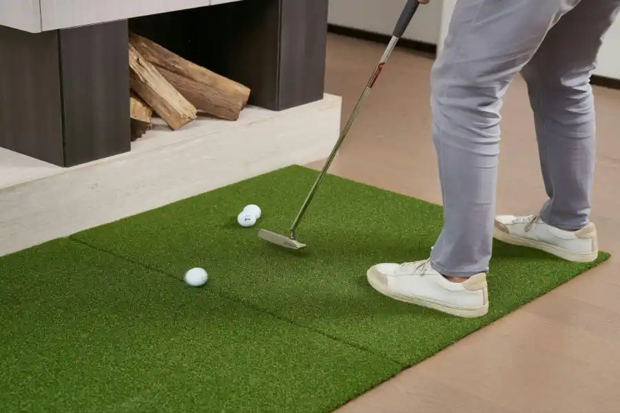 Person practicing golf indoors on an artificial turf mat near a fireplace.
