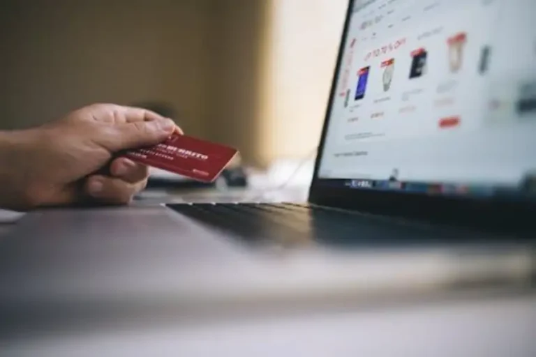 Hand holding a credit card while shopping online on a laptop.