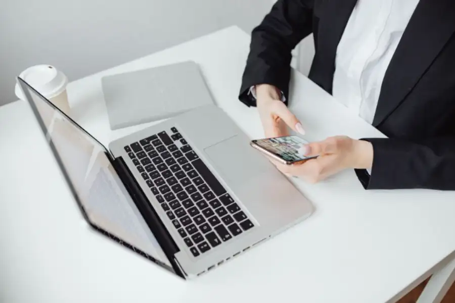 Businesswoman using a smartphone beside a laptop on a clean office desk.